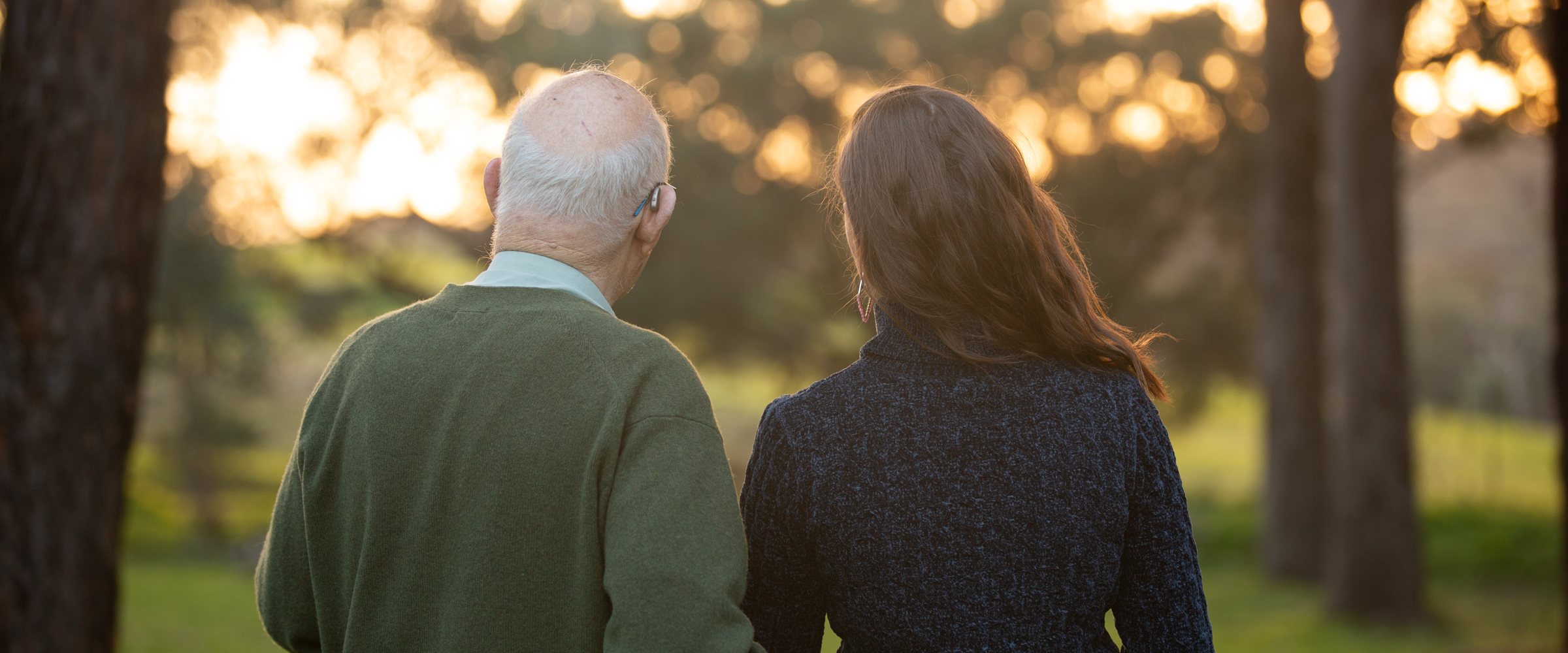 David Cummings and Tahlia Field walking together among trees at sunset, seen from behind